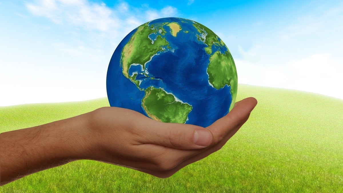 hand holding the Earth in front of green sunny background